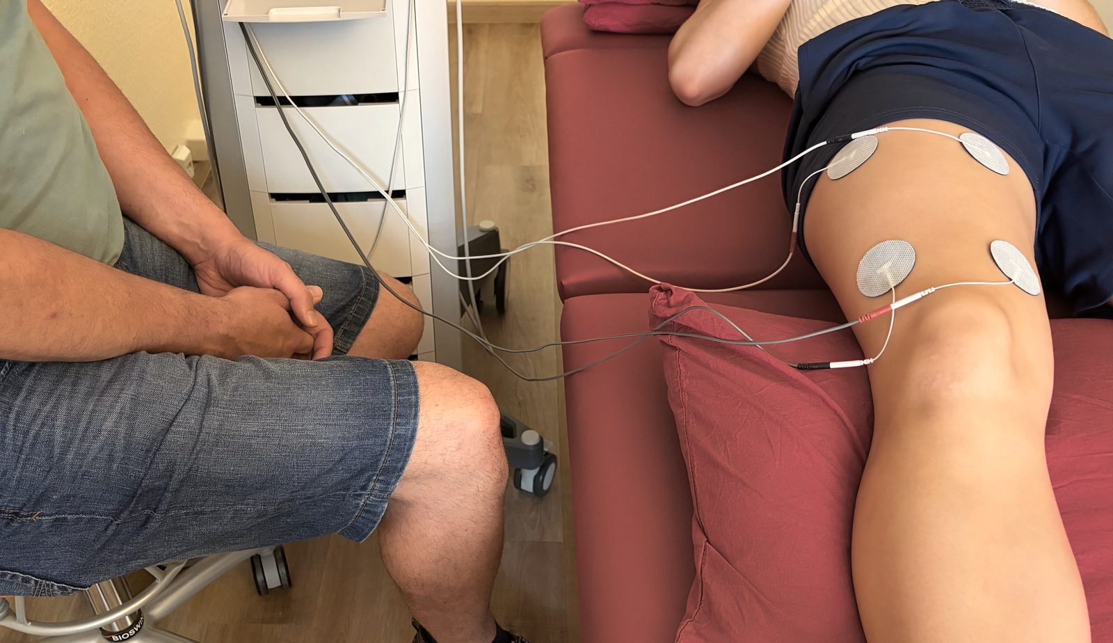 Elektrotherapie am Knie: ein Therapeut begleitet die Behandlung, Elektroden liegen auf dem Gelenk