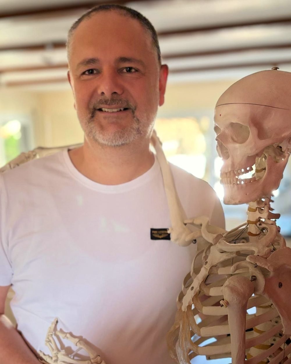 Porträt von Marko Tanin neben einem anatomischen Skelettmodell