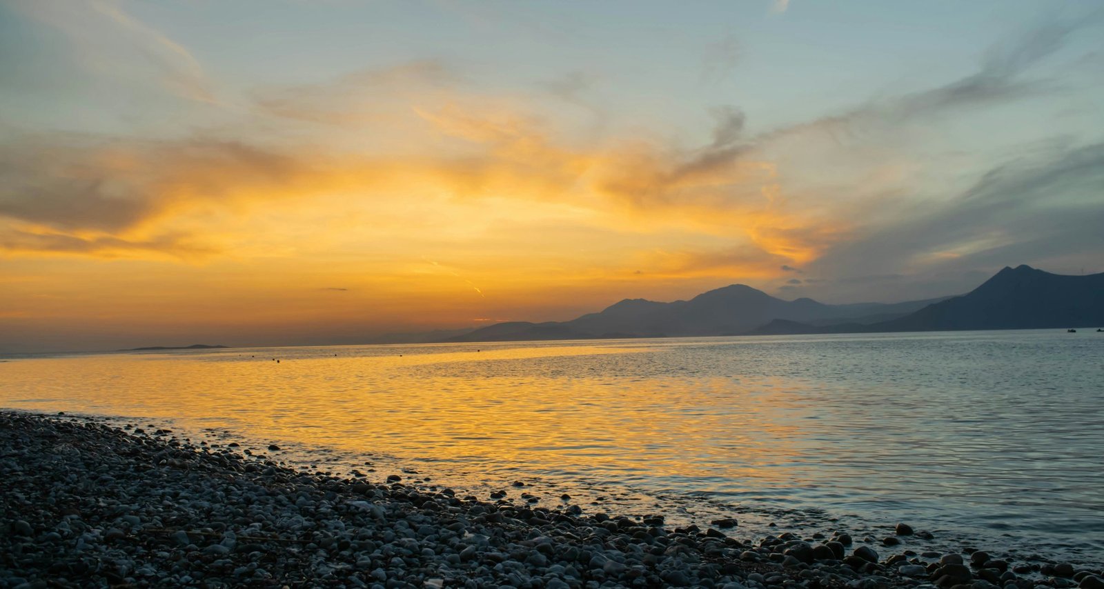 Sonnenuntergang über dem Meer, im Vordergrund ein Kieselstrand